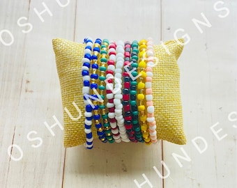 May include: A set of colorful beaded bracelets, stacked on a yellow cushion. The bracelets are made of small, round beads in various colors, including blue, green, red, white, and yellow.