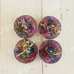 May include: Four purple tea light candles with dried flowers and gold glitter embedded in the wax.
