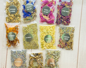 May include: A collection of ten small, clear plastic bags filled with dried herbs and flowers. Each bag has a gold label with text, including "Sophore Flower," "Forget-Me-Not," "Peony Petals," and "Rose Buds." Other labels read "Marigold," "Rosemary," "Jasmine," "Spiritual Herbs," "Lavender," "Witchy Herbs," and "Sage."
