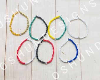 May include: Seven colorful beaded bracelets with a silver charm on each. The bracelets are red, white, black, yellow, green, white, and blue.