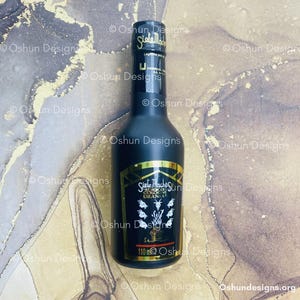 Puede incluir: Una botella de colonia negra con detalles dorados y el texto "Siete Machos Cologne Urania". La botella tiene una capacidad de 110 ml. El fondo presenta un diseño veteado con tonos dorados y marrones.