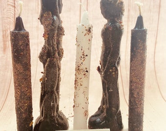 May include: Four black and white candles, two of which are shaped like figures, with a white background and a sign that reads "SHUN DESIGNS".