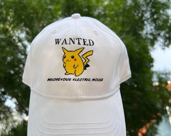May include: White baseball cap with embroidered text and a yellow Pikachu graphic. The text reads "WANTED" above the Pikachu image, with "MISCHIEVOUS ELECTRIC MOUSE" below. The cap is held up against a green leafy background.