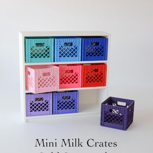 May include: A white three-tiered shelving unit containing eight colorful plastic mini milk crates in shades of teal, light blue, dark blue, light pink, hot pink, red, light purple, and dark purple, with one dark purple crate placed in front.