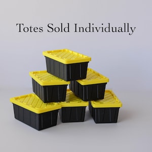 May include: Stack of six black storage totes with yellow lids. The totes are rectangular and have a textured lid design. The text "Totes Sold Individually" is above the totes.
