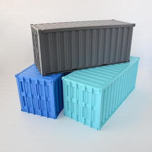 May include: Three rectangular shipping container models stacked together. The top container is dark gray, while the two bottom containers are blue and light turquoise. Each model features vertical corrugated walls and detailed door panels.