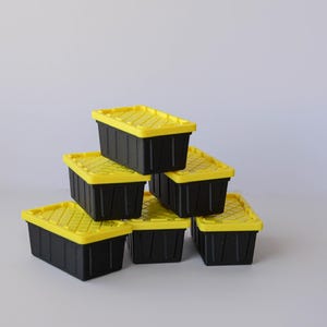 May include: Six black storage bins with bright yellow lids are stacked in a pyramid shape. The bins are rectangular with a textured lid design. The background is a plain white.