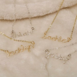 May include: Four delicate gold and silver necklaces with personalised names, "Insan", "Sachie", "Jacklyn", and "Gaibby", are displayed on a soft, beige, fuzzy surface.