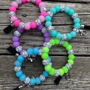 May include: Four colorful silicone beaded bracelets with a smiley face design. Each bracelet has a black tassel and a silver key ring.
