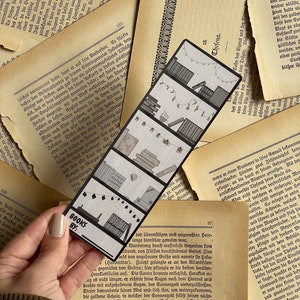 May include: A black and white bookmark with a design of books, a cup of coffee, and string lights. The bookmark has the text "BOOKS BY:" at the bottom.