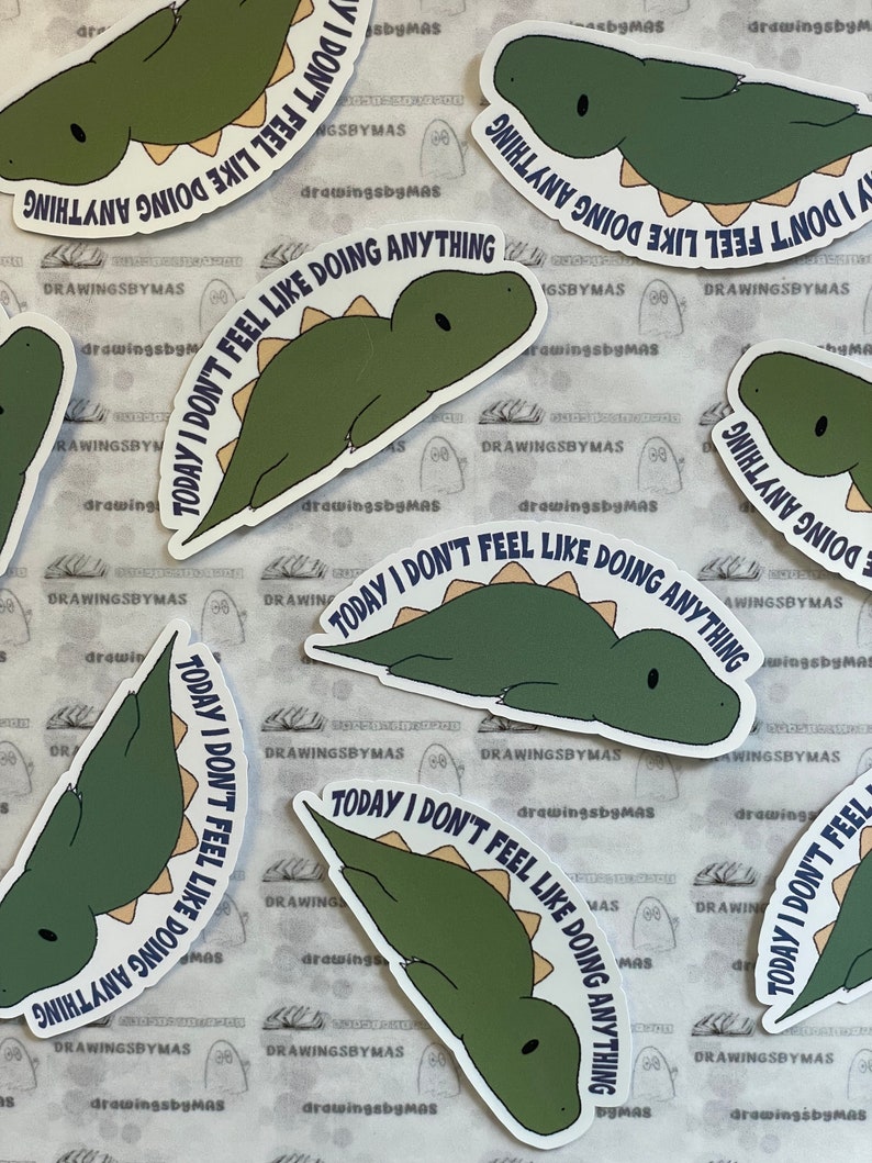 Puede incluir: Una colecci&oacute;n de pegatinas con un dinosaurio de dibujos animados en tonos verdes y beige. Cada pegatina tiene el texto "TODAY I DON'T FEEL LIKE DOING ANYTHING" en una fuente azul oscuro. Las pegatinas est&aacute;n dispersas sobre una superficie estampada.