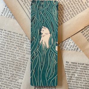 May include: A white cat with green eyes peeks out from behind tall green grass. The cat is looking to the right of the image. The background is a dark green.