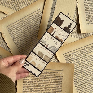 May include: A bookmark with a black and white design featuring a series of four rectangular panels. Each panel depicts a different scene with a black and white color scheme. The bookmark is labeled "BOOKS BY:" at the bottom.