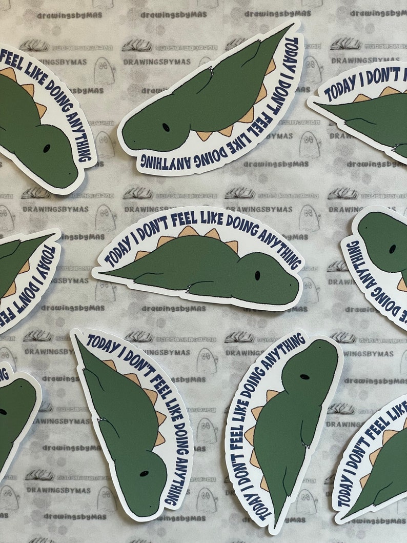 Puede incluir: Un conjunto de pegatinas con un dinosaurio de dibujos animados verde y beige. El texto "TODAY I DON'T FEEL LIKE DOING ANYTHING" en azul marino rodea al dinosaurio. Las pegatinas est&aacute;n sobre un fondo estampado.