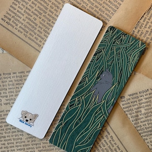 May include: Two bookmarks, one with a white background and a cartoon dog peeking out from the bottom, and the other with a green and yellow leafy pattern and a gray cat peeking out from the top.