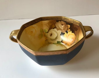 May include: A blue and gold octagonal serving bowl with two handles. The bowl is decorated with a floral pattern of white and yellow roses.