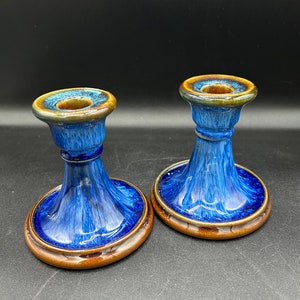 May include: A pair of blue and brown ceramic candle holders. The holders have a flared base and a small, round top.