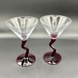 May include: Two clear glass martini glasses with a twisted, dark red stem and base.