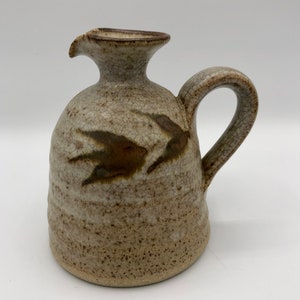 May include: A small, brown and white ceramic jug with a brown bird design. The jug has a handle and a spout.