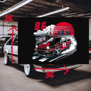 Peut inclure: Un t-shirt noir avec une illustration rouge et blanche d'une voiture dérivant sur une piste de course. La voiture porte le numéro "2" et le texte "AE86". L'arrière-plan comprend un soleil rouge et une ville.