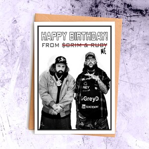 May include: Black and white birthday card with the text "HAPPY BIRTHDAY! FROM $ORIM & RUBY ME". The card features two men in casual attire, with hats and jewelry. The card is inside a brown envelope.