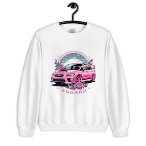 May include: White sweatshirt featuring a pink Subaru car graphic. The car is surrounded by flowers and a crescent moon. The text "SUBARU" is printed below the car.