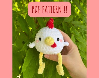 May include: A white crocheted chicken amigurumi with red comb, yellow beak, and yellow legs. The chicken is being held in a hand against a green leafy background. The text "PDF PATTERN!!" is written in a pink box above the chicken.