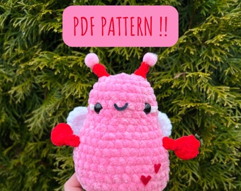 Peut inclure: Un jouet amigurumi en crochet rose avec des bras et des jambes rouges, des ailes blanches et deux cœurs rouges sur le dos. Le jouet a un visage souriant avec des yeux noirs et une bouche noire. Le texte "PDF PATTERN!!" est écrit en rouge sur un fond rose.