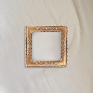 May include: A square picture frame with a metallic gold finish and a beaded inner and outer border. The frame features embossed silver-toned floral vine accents centered on each of the four sides, surrounding a plain white rectangular center.