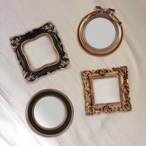 May include: Four ornate picture frames in various shapes. One is square with a gold finish, another is round with a bow detail, and a third is a black square with gold accents. The fourth frame is a black and gold circle.