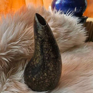 Könnte beinhalten: Eine schwarze und goldene Keramikvase mit einer einzigartigen, asymmetrischen Form. Die Vase hat eine gesprenkelte, strukturierte Oberfläche.