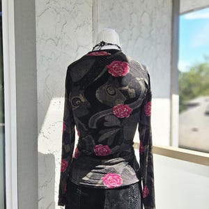 May include: A black top and skirt set on a mannequin. The top features a floral design in pink and grey, with long sleeves. The skirt is black and has a patchwork design, possibly suede.