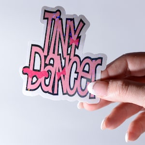 May include: A pink and white sticker with the text "Tiny Dancer" in a glittery font.