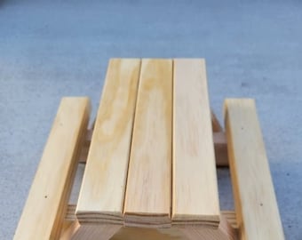May include: A small wooden picnic table with two benches. The table is made of unfinished wood and has a natural wood colour.