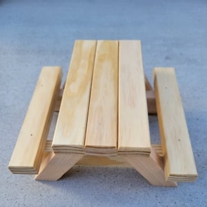 May include: A small wooden picnic table with two benches. The table is made of unfinished wood and has a natural wood color.