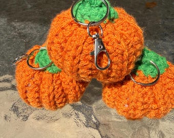 May include: Three handmade crochet pumpkin keychains. The pumpkins are orange with green stems and silver key rings. The keychains are made of yarn and are a fall-themed accessory.