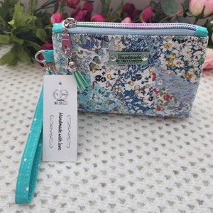 May include: A small, blue and white floral print zippered pouch with a turquoise wrist strap and a tag that reads "Handmade with love".