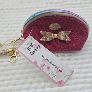 May include: A burgundy coin purse with a gold zipper and a bow accent. The purse has a gold keychain with a tassel. A tag reads "Y&B's Creations" and "Handmade with love".