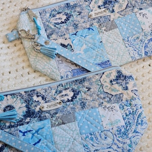 May include: Two blue and white patchwork fabric zippered pouches with tassels and a silver zipper pull. The pouches have a "Handmade" label on them.