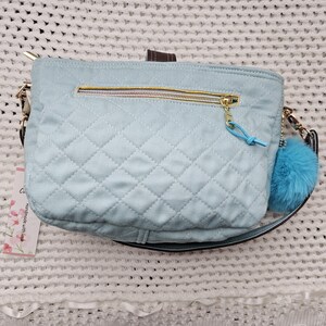 May include: A light blue quilted shoulder bag with a gold zipper and a fluffy blue charm. The bag has a black strap and a gold buckle.