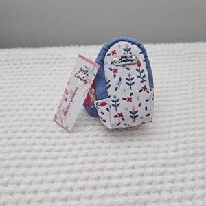 May include: A small, blue and white floral patterned backpack-shaped coin purse. The purse has a zipper closure and a tag that reads "Y&B's Creations, Handmade with love."