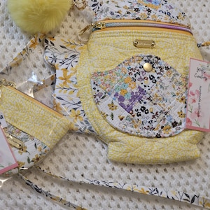 May include: A yellow quilted crossbody bag with a floral print and a smaller matching zippered pouch. The bag has a strap and a label that says "Y&B's Creations Handmade with love".