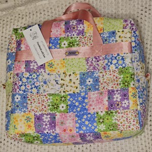 May include: A patchwork tote bag with a pink ribbon handle and a tag that reads "Handmade with love". The bag is made of different floral fabrics in shades of pink, blue, yellow, and green.