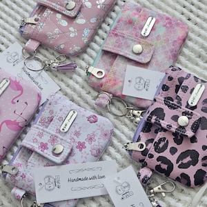 May include: Five pink and white fabric coin purses with zipper closures and keychains. Each purse has a different pattern and a silver name tag with the text "Handmade with love".