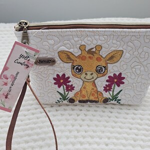May include: White zippered pouch with a giraffe applique and embroidered flowers. The pouch has a brown zipper and a brown wrist strap. The tag reads "Y&B's Creations Handmade with love."