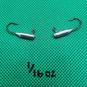 Puede incluir: Dos cabezas de anzuelo de pesca plateadas con anzuelos, cada una con un peso de 1/16 oz, se muestran sobre un fondo verde texturizado. Los anzuelos son curvos y las cabezas de anzuelo son cilíndricas. El texto "1/16 oz" está impreso en negro.