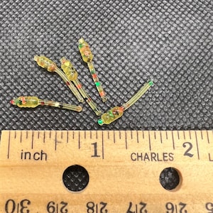 May include: Five small, translucent yellow plastic fishing lures with segmented bodies and embedded multi-colored flecks. The lures are positioned above a wooden ruler, showing each piece measures approximately 0.75 inches in total length.
