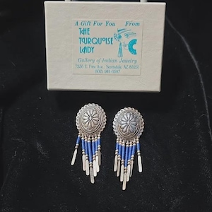 Könnte beinhalten: Silberfarbene Ohrringe mit floralem Design und blauem Perlenbesatz. Die Ohrringe werden mit einer Geschenkbox präsentiert, auf der steht: "A Gift For You From The Turquoise Lady, Gallery of Indian Jewelry."