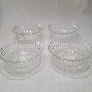May include: Set of four clear glass bowls with a decorative, embossed pattern. The bowls are round and have a fluted edge.