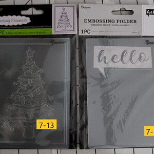 May include: Two clear plastic embossing folders, one with a Christmas tree design and the text "7-13" and the other with a tree design and the text "hello" and "7-14".